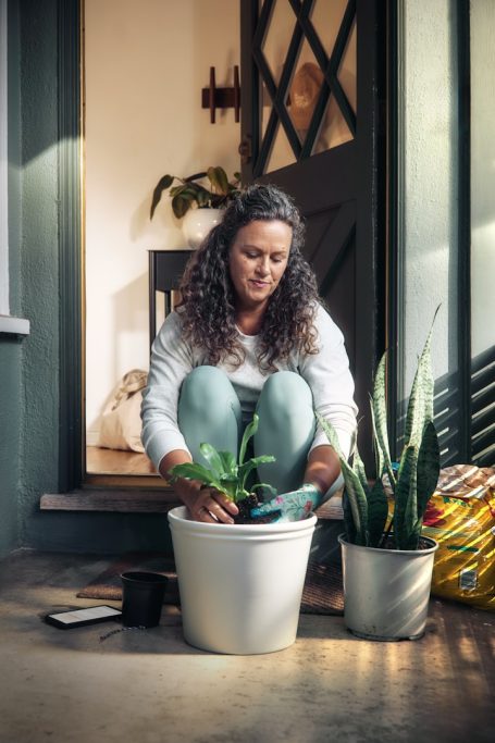 Gleichgewicht Eine Frau sitzt auf dem Boden und pflanzt eine Blume in einen Blumentopf