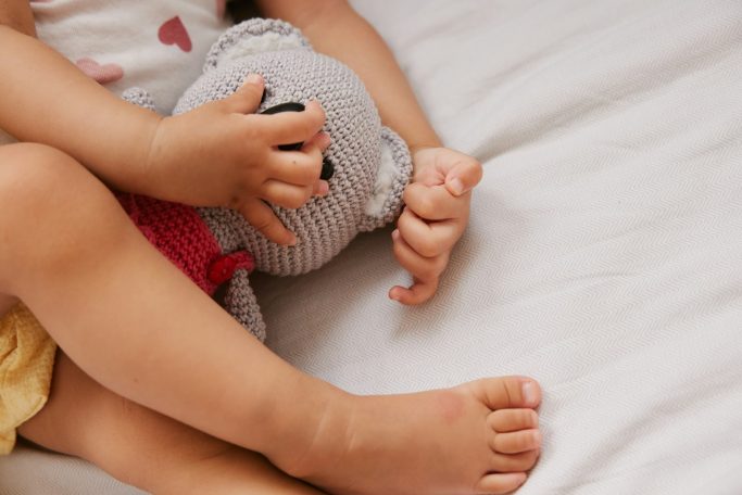 Pull Babyhände ziehen eineen gehäkelten Bären an den Körper