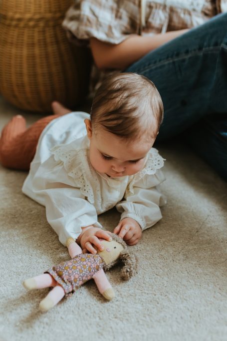 Grasp Ein Baby liegt auf dem Bauch und greift eine Stoffpuppe, die vor ihm liegt.