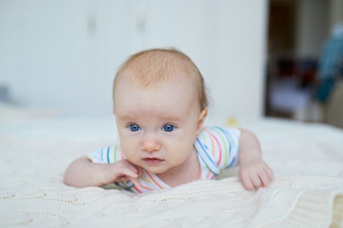 Push Ein Baby von wenigen Monaten liegt auf dem Bauch auf einer Decke und hebt den Kopf.
